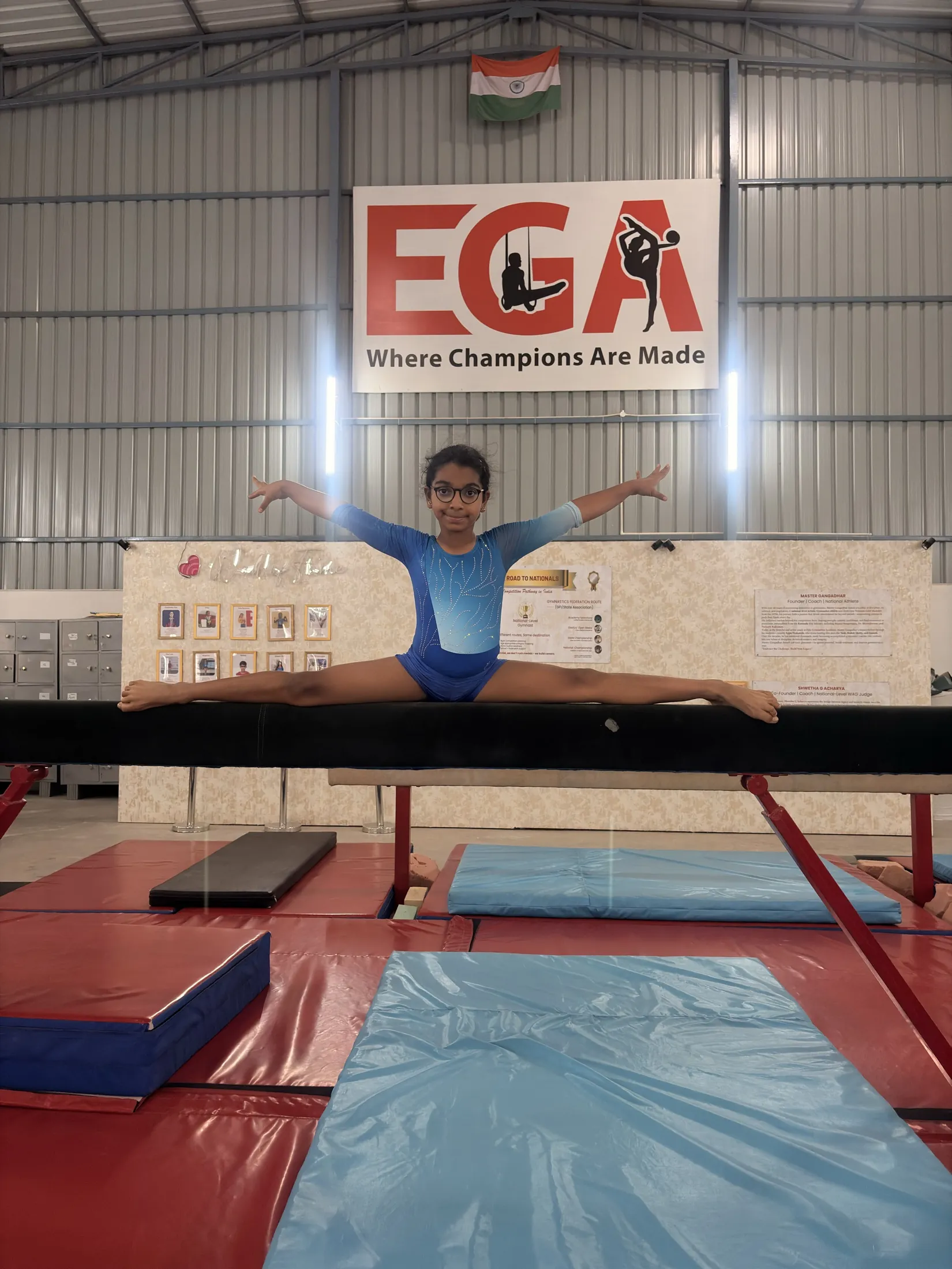 Young gymnast in a split on the balance beam beneath the EGA banner