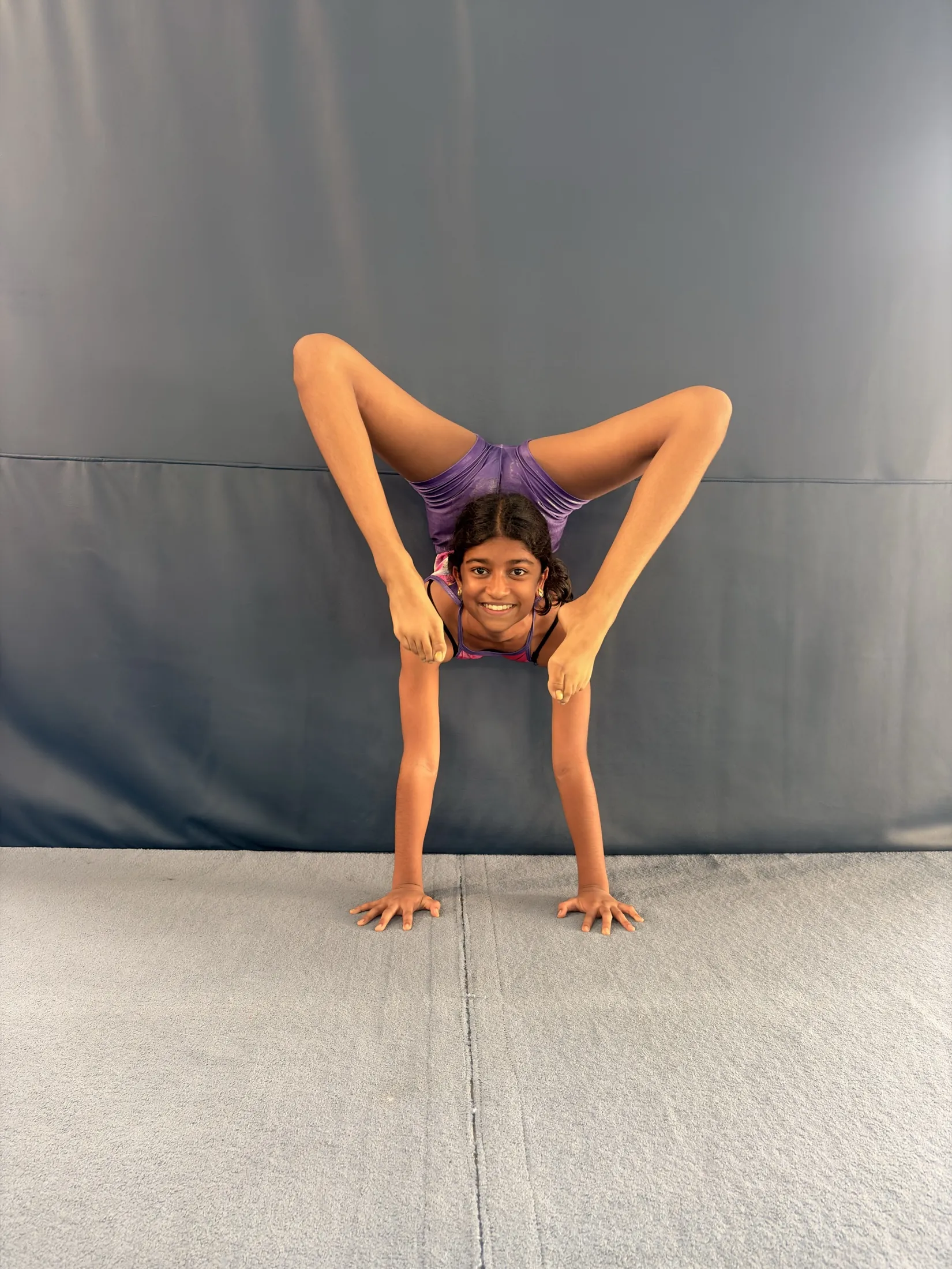 Smiling gymnast in a handstand straddle